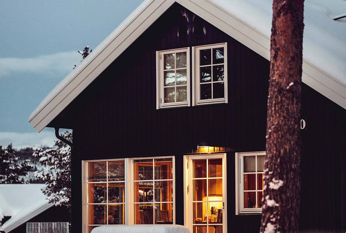 Pest-proofing a home in the new year – black and white house with snow, tree in front, light inside seen through windows and door